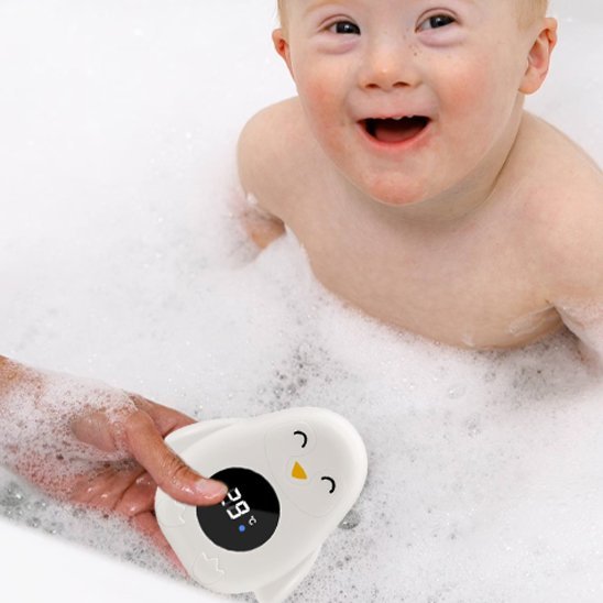 Thermomètre bain bébé bébé qui rit en tenant son thermomètre assis dans son bain